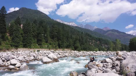 Aerial-shot-of-water-stream-flowing-near-the-rocks-and-mountain-in-the-background