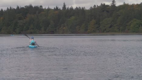 Kayaker-paddling-away-wide-shot-beautiful-scenic-river-view