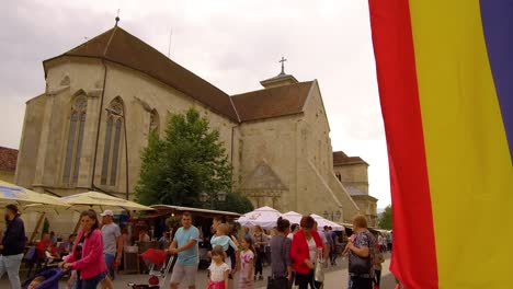 Downwards-panning-shot-of-crowd-walking-in-front-of-Romanina-Church-with-the-Flag-drapsed-on-the-right-of-the-frame