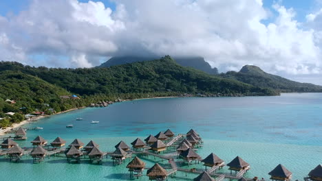 Toma-Panorámica-Aérea-De-Las-Montañas-De-Bora-Bora-Y-Los-Bungalows-Sobre-El-Agua-En-El-Océano-Pacífico,-Bora-Bora,-Polinesia-Francesa.