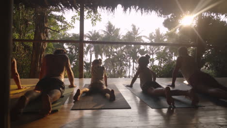 Deslícese-A-Lo-Largo-De-Una-Familia-De-Viajeros-Que-Disfrutan-De-Una-Meditación-Al-Atardecer-Y-Una-Sesión-De-Yoga-En-Un-Porche-De-Madera-Con-Vista-A-La-Selva-Tropical-Y-La-Jungla-Que-Conduce-A-La-Playa