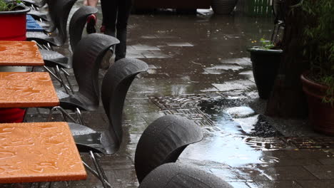 Starker-Regen-Auf-Der-Terrasse-Eines-Cafés,-Spaziergänger-Eilen-Vorbei