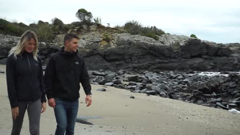 SLOWMO---Boyfriend-and-girlfriend-walking-on-beach-in-Bluff,-New-Zealand-on-cloudy-day