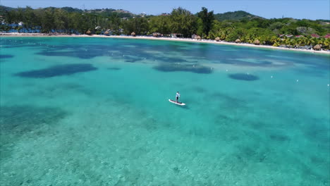 Vista-Aérea-En-Cámara-Lenta-De-Personas-Practicando-Remo-Cerca-De-La-Playa-De-Un-Resort-En-El-Mar-Caribe-Hondureño