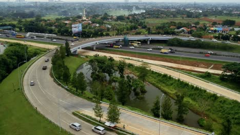 Enthüllung-Einer-Luftdrohnenaufnahme-Einer-Kurvigen-Autobahn,-Einer-Brücke-Und-Eines-Kleinen-Sees-Mit-Grünen-Bäumen-Bei-Alam-Sutera-Am-Tag