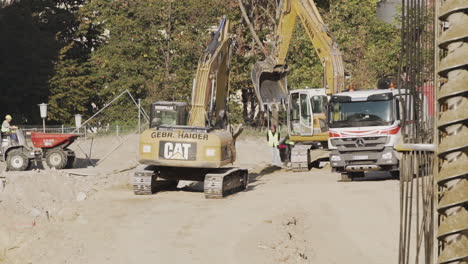 Excavadora-Trabajando-En-Un-Sitio-De-Construcción-En-Viena,-Austria-Con-Personas-Y-Un-Camión-Al-Lado-Ocupado-Trabajando