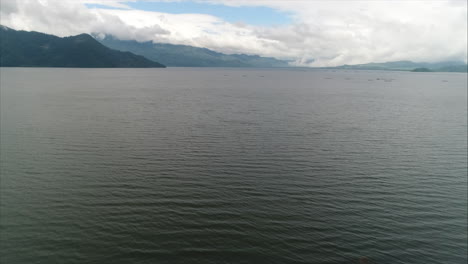 AERIAL:-Panoramic-shot-of-lake-sorrounded-by-mountains-and-blue-sky,-Yojoa,-Honduras