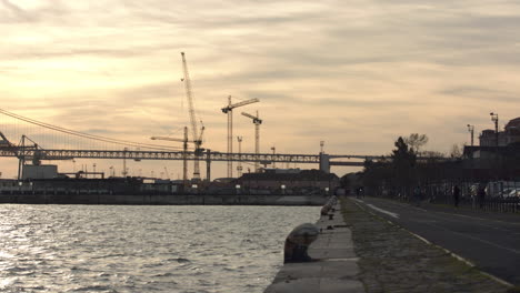 Menschen,-Die-Im-Sonnenuntergang-Am-Fluss-Tejo-In-Der-Nähe-Der-Brücke-Vom-25.-April-Spazieren-Gehen