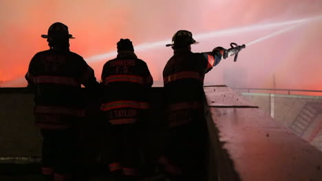 A-Firefighter-Sprays-a-Hose-Onto-a-Fire-from-a-Rooftop,-Close-Up-Static-Shot