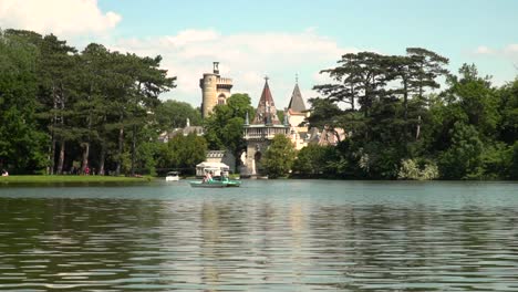 Blick-Auf-Das-Schloss-Laxenburg-Hinter-Dem-See-Mit-Vorbeifahrenden-Booten-An-Einem-Hellen-Und-Sonnigen-Sommertag