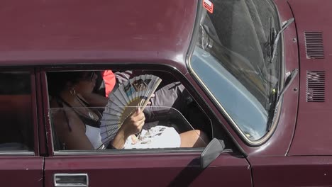 Mujeres-Cubanas-Sentadas-En-El-Asiento-Del-Pasajero-De-Un-Auto-Antiguo-Rojo-Mientras-Usan-Un-Ventilador-De-Mano-Para-Refrescarse-La-Cara-En-Un-Día-Caluroso-Y-Soleado-En-La-Ciudad-De-La-Habana