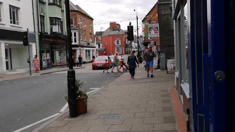 Family-with-buggy-crossing-road,-and-pedestrians-walking-down-shopping-street