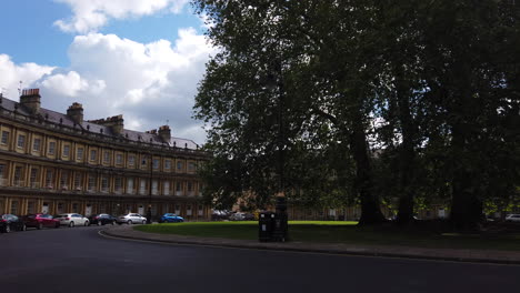 Der-Zirkus-In-Bath,-Somerset-An-Einem-Sommertag-Mit-Blauem-Himmel-–-Weiße-Wolken-Und-Verkehr,-Der-Durch-Das-Bild-Schwenkt,-Von-Links-Nach-Rechts