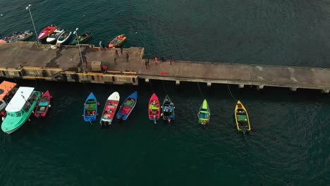 Un-Mercado-De-Pescado-Local-Con-Pescadores-Vendiendo-Desde-Los-Barcos-Junto-Al-Embarcadero-Con-Montañas-Y-Playas-Al-Fondo