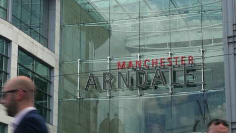 Arndale-Shopping-Centre-Manchester-City-Centre-Nahaufnahme-Des-Schildes-An-Einem-Sonnigen-Sommertag-Mit-Passanten-Davor,-Nahaufnahme-4k-25p