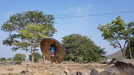 A-man-carrying-a-coracle-and-a-paddle,-and-walking-on-a-bright-sunny-day-with-the-sky-and-trees-in-the-background-in-Hogenakkal,-Tamilnadu,-India