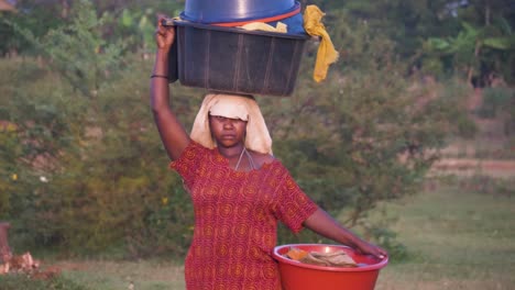 Nahaufnahme-Einer-Afrikanerin-In-Zeitlupe,-Die-Im-Ländlichen-Afrika-Eine-Eimerladung-Kleidung-Auf-Ihrem-Kopf-Balanciert