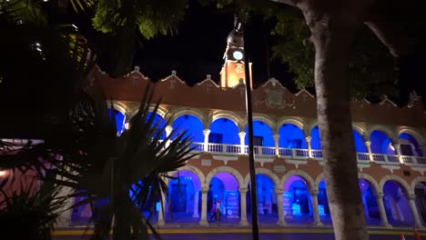 Dolly-Shot-A-La-Izquierda-Del-Edificio-Municipal-Al-Atardecer-Con-Sus-Luces-Azules-Al-Lado-De-La-Plaza-Grande-En-Merida,-Mexico