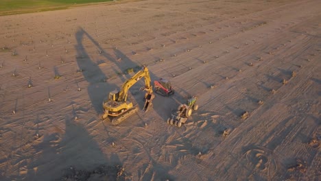 Toma-Aérea-De-Una-Retroexcavadora-Y-Una-Carretilla-Elevadora-Estacionada-En-Un-Campo-Vacío-Durante-La-Hora-Dorada