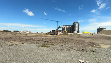 Established-shot-of-construction-site,-excavator-and-heavy-machinery-in-action-loading-sand-in-truck,-building-condominiums,-land-and-beautiful-sky