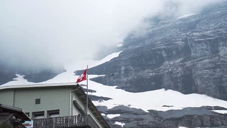 Schweizer-Flagge-Weht-Dramatisch-Mit-Vögeln,-Die-In-Zeitlupe-Am-Eigergletscher-Fliegen