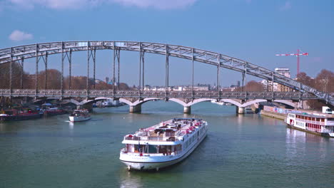 A-large-and-a-small-ship-cross-underneath-the-Viaduc-d'Austerlitz-in-Paris-on-a-sunny-day-at-noon