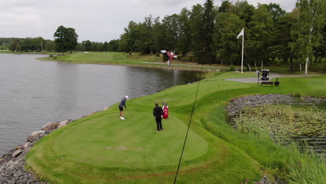 Aerial-arc-shot-of-golfer-and-caddie-on-a-beautiful-golf-course-with-a-lake-in-the-background