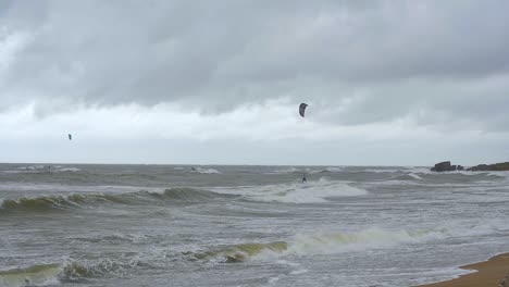 Kite-surfing-surfers-sailing-on-the-big-Baltic-sea-waves-at-Liepaja-Karosta-beach,-overcast-autumn-day,-slow-motion-wide-shot