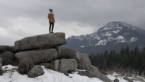 A-girl-stands-on-boulders-with-snowy-mountains-around-her