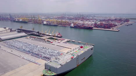 Aerial-view-of-logistics-concept-of-commercial-vehicles,-cars-and-pickup-trucks-waiting-to-be-load-on-to-a-roll-on-roll-off-car-carrier-ship