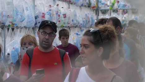 Exposición-Sobre-El-Cambio-Climático,-Gente-Caminando-A-Través-De-Una-Exhibición-De-Arte-De-Botellas-Recicladas-Colgadas