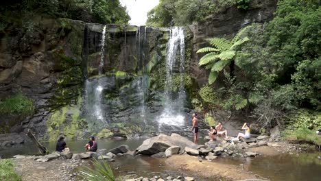 Slowmo---Grupo-De-Jóvenes-Sentados-Junto-A-Las-Cataratas-De-Mokora,-Auckland,-Nueva-Zelanda