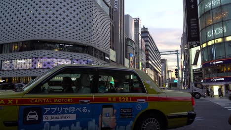Taxi-Stopped-At-The-Road-In-Ginza-Japan-Waiting-For-The-Traffic-Light-Signal-To-Go-With-Modern-Buildings-In-The-Background-At-Sunset--Closeup-Shot