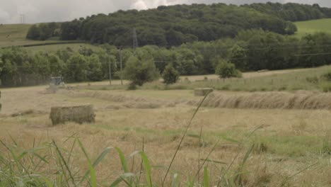 Landschaft-Mit-Heuballenfeld-Und-Traktor-In-Der-Ferne