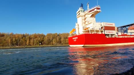 Barco-De-Contenedores-Rojo-Que-Transporta-Carga-En-Un-Río-Claro,-Cielo-Soleado