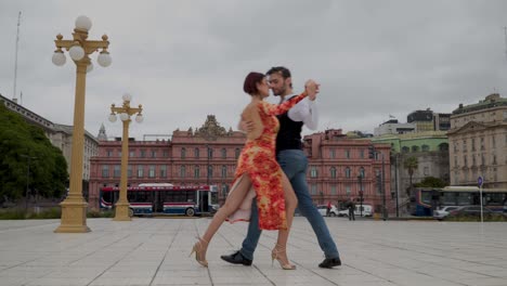 Zwei-Erfahrene-Tangotänzer-Führen-Eine-Schwierige-Routine-Auf-Einem-Platz-In-Buenos-Aires-Mit-Casa-Rosada-Im-Hintergrund-Durch