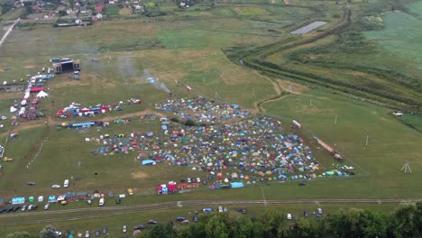 Vista-Aérea-De-Carpas-Multicolores-Colocadas-En-Un-Campo-En-Un-Festival-De-Música-Con-La-Ciudad-En-Segundo-Plano