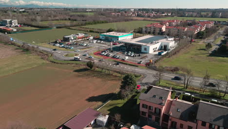 Vista-Aérea-Del-Tráfico-Que-Conduce-A-Lo-Largo-De-La-Zona-Comercial-Con-Mercado-De-Alimentos,-Comida-Rápida-Y-Tiendas-Cerca-De-La-Zona-Residencial-En-Arcore,-Norte-De-Italia