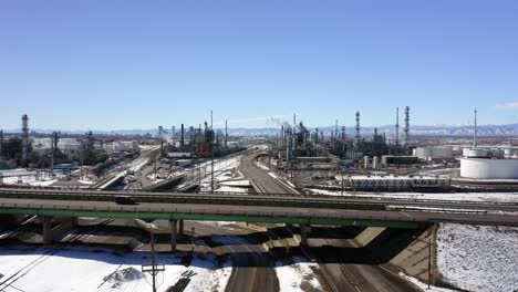 La-Vista-Aérea-Se-Mueve-Hacia-Arriba-Para-Mostrar-Una-Refinería-Y-Una-Autopista-Con-El-Centro-De-Denver-Y-Las-Montañas-Al-Fondo