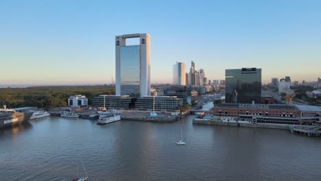 Dolly-Aéreo-Fuera-De-Los-Barcos-Que-Navegan-En-Los-Muelles-De-Puerto-Madero-Con-Rascacielos-En-El-Fondo-Al-Atardecer,-Buenos-Aires