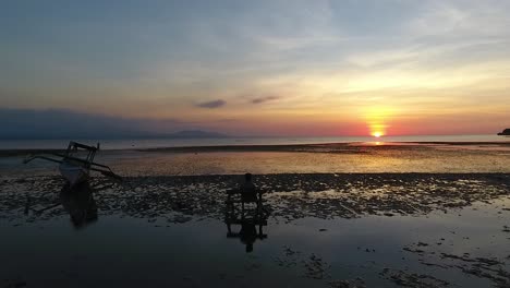 Mann-Auf-Einer-Bank-Am-Meer-Beobachtet-Das-Wasser,-Das-Den-Subtilen-Schein-Des-Pastellfarbenen-Sonnenuntergangs-Reflektiert