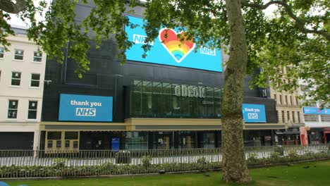 Encierro-En-Londres,-Hombre-Sin-Hogar-En-Leicester-Square-Duerme-Frente-Al-Cine-Odeon-Cerrado-Con-Carteles-De-Gracias-Nhs,-Durante-La-Pandemia-De-Coronavirus-2020