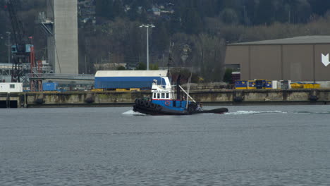 Tug-boat-cruising-on-sea-with-industrial-harbor-in-background