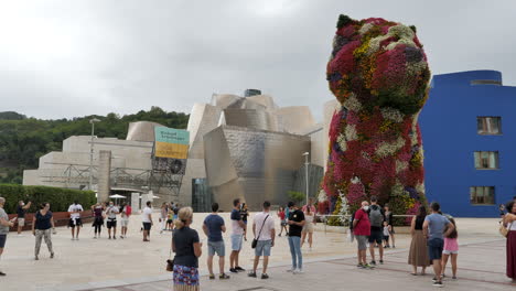 Tourists-At-The-Guggenheim-Museum-In-Bilbao,-Spain-With-The-World's-Largest-Flower-Structure-Of-Puppy-In-Front---full-shot