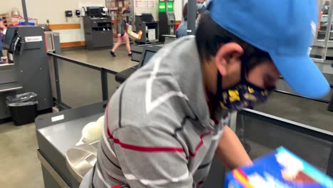 Young-Asian-boy-wearing-face-mask-scanning-grocery-item-at-self-checkout-counter-in-Costco