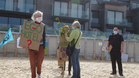 Women-demonstrating-on-the-beach-in-front-of-the-Carbis-Bay-Hotel-in-St-Ives,-Cornwall,-whilst-man-looks-on