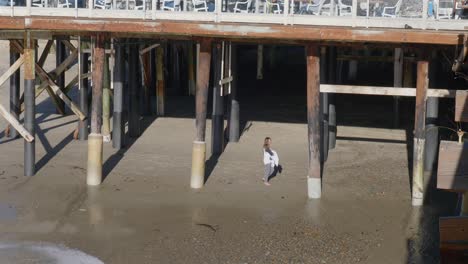 Toma-Panorámica-De-Una-Niña-Debajo-De-Un-Muelle-Hasta-El-Patio-Del-Restaurante-Arriba