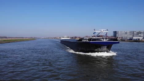 Vessel-Yemaya-Cargo-Ship-Sailing-Under-The-Waving-Flag-Of-Netherlands-In-Noord-River-With-Cityscape-In-Background