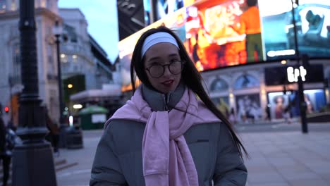 Beaufitul-young-woman-touches-her-hair,-looks-at-the-camera-in-Picadilly-Circus