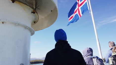 Ondeando-La-Bandera-Nacional-De-Islandia-En-El-Barco-Mientras-La-Gente-Admira-La-Vista,-Inclina-La-Vista-Hacia-Abajo